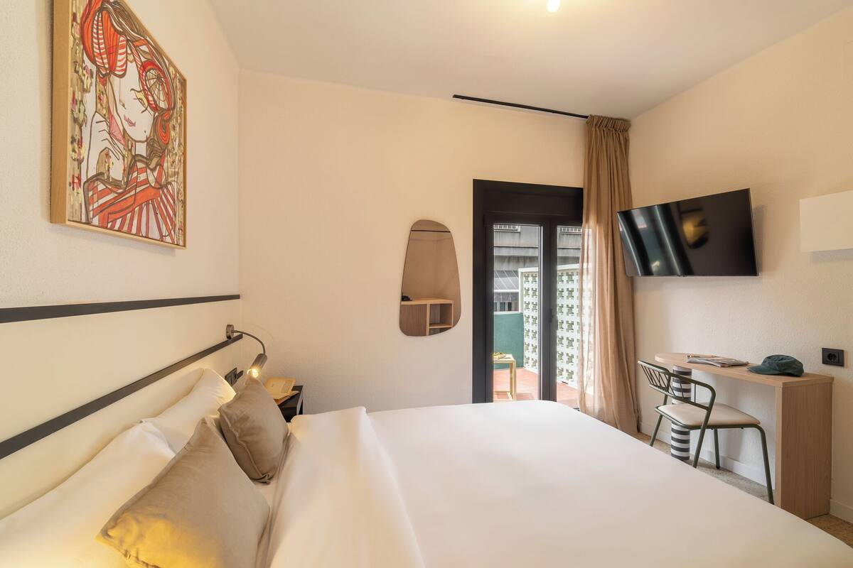A hotel room with a bed, a desk, a chair, a TV, and a painting on the wall.