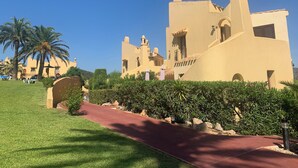 A large, beige building with multiple towers and arched windows, surrounded by well-maintained greenery and a red pathway. - Beautiful, comfortable home in the heart of the sought-after Manga Club (Cartagena)
