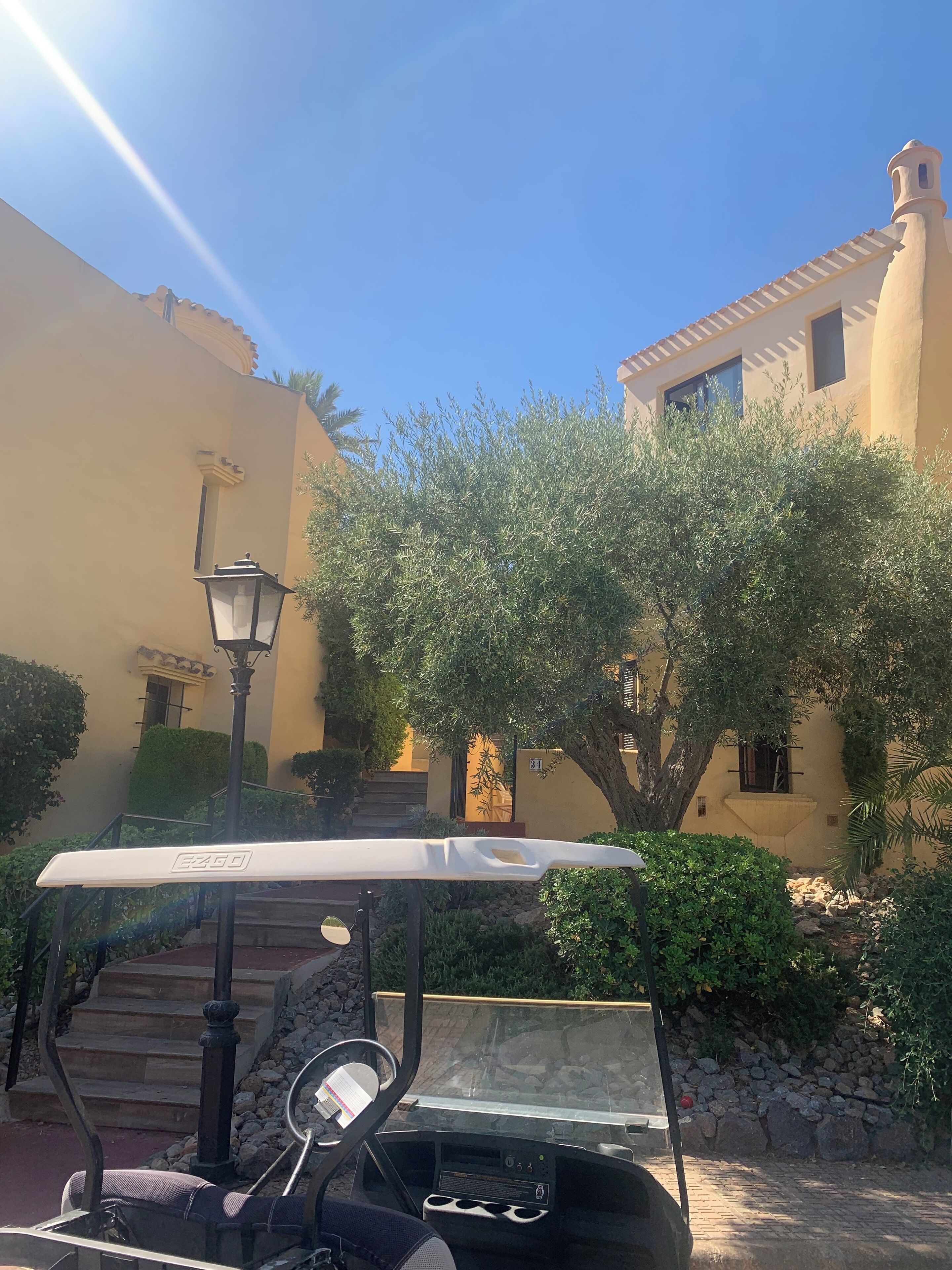 Une voiturette de golf est garée dans une cour, près d’un lampadaire, d’un escalier et d’un bâtiment dont le toit est recouvert de tuiles.