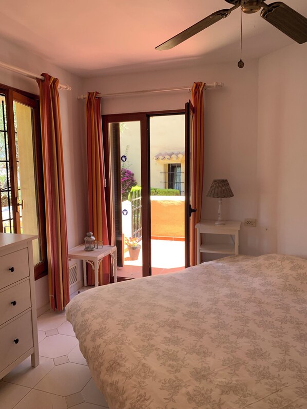 A bedroom with a bed, a desk, a lamp, and a view of the outside.