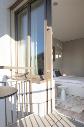 Un balcón con mesa y sillas, una cama con almohadas y vistas al exterior.