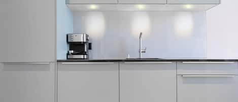 Une cuisine moderne avec des meubles blancs, une machine à café et un robinet en acier inoxydable.
