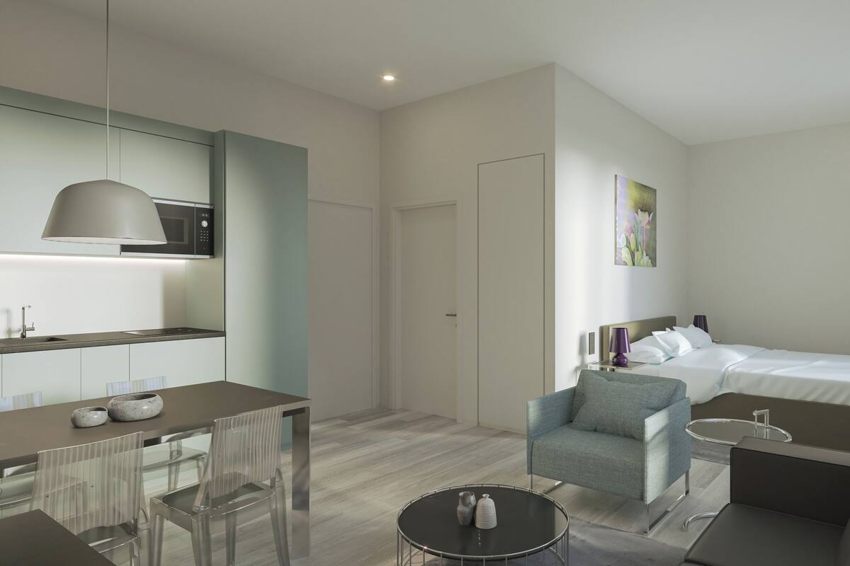 A modern hotel room with a dining area, a sofa, a bed, and a small round table.