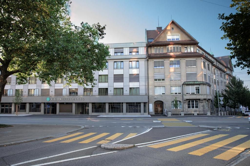 Un edificio de varios pisos con fachada moderna, una entrada visible y un paso de peatones enfrente.