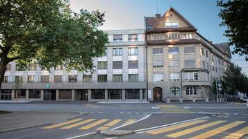A multi-story building with a modern facade, a visible entrance, and a crosswalk in front.