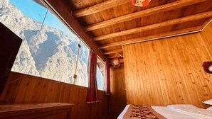 Una habitación de madera con una cama, un banco de madera y una ventana con vista a la montaña.