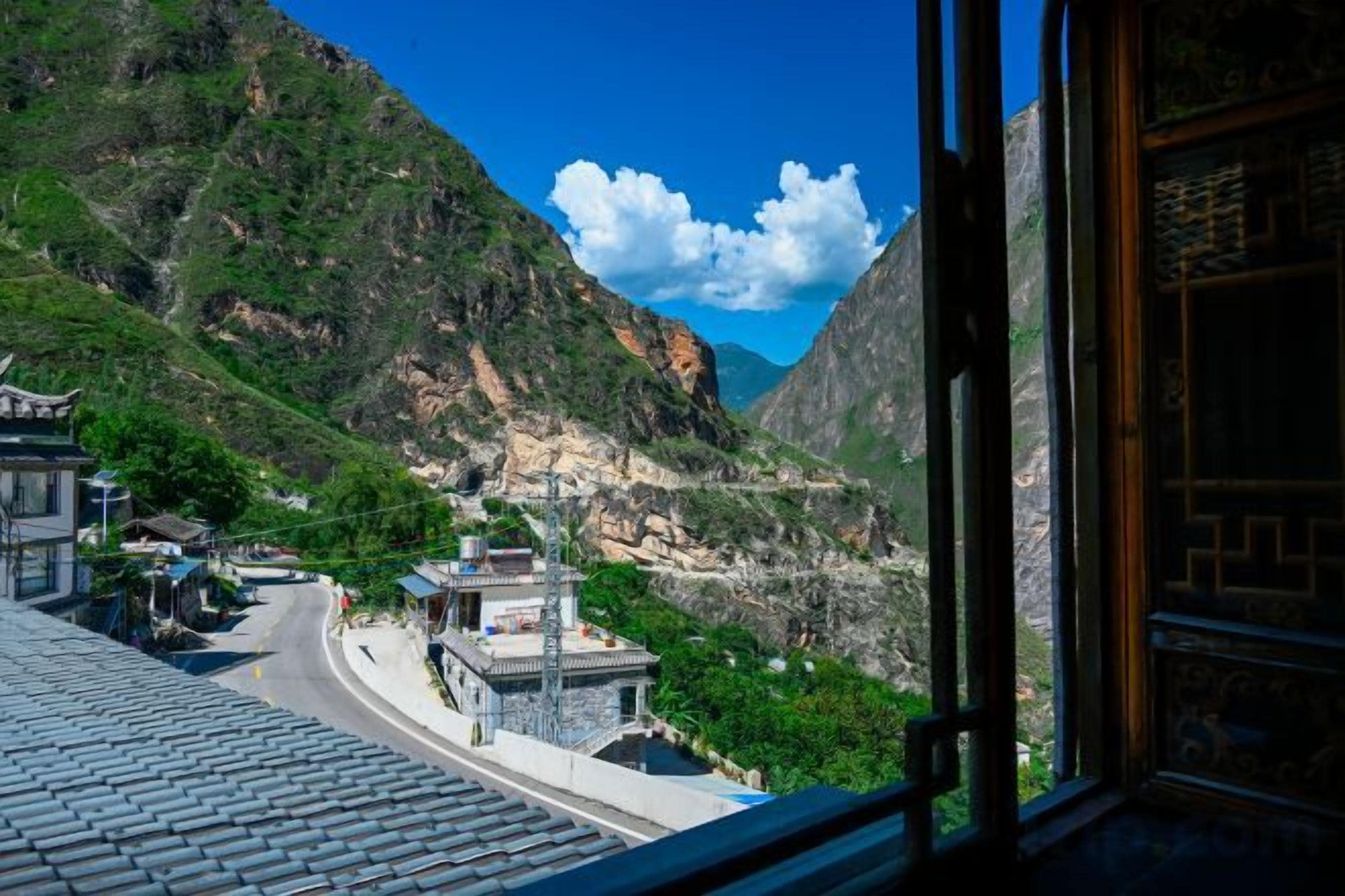 Paesaggio montuoso con una strada, edifici tradizionali e cielo sereno.