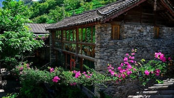 A traditional stone building with a tiled roof, large windows, and a staircase leading to the entrance.