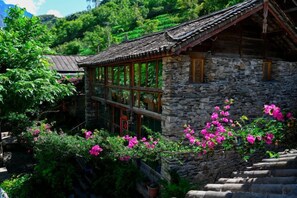 A traditional stone building with a tiled roof, large windows, and a staircase leading to the entrance.