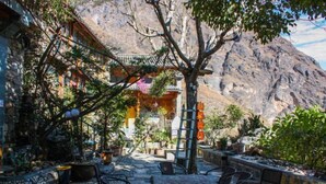 Un área de estar al aire libre con mesas y sillas de piedra, rodeada de plantas en macetas y un paisaje montañoso.