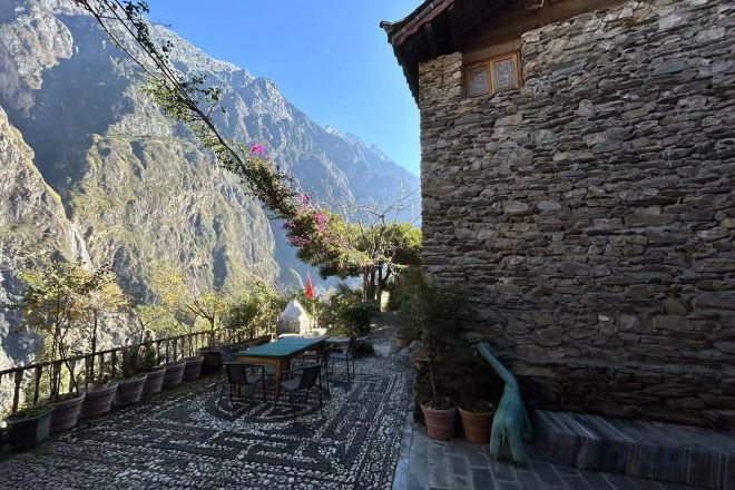 A stone building with a terrace, outdoor seating, and a mountain view.