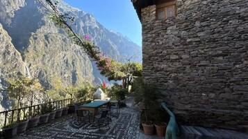 A stone building with a terrace, outdoor seating, and a mountain view.