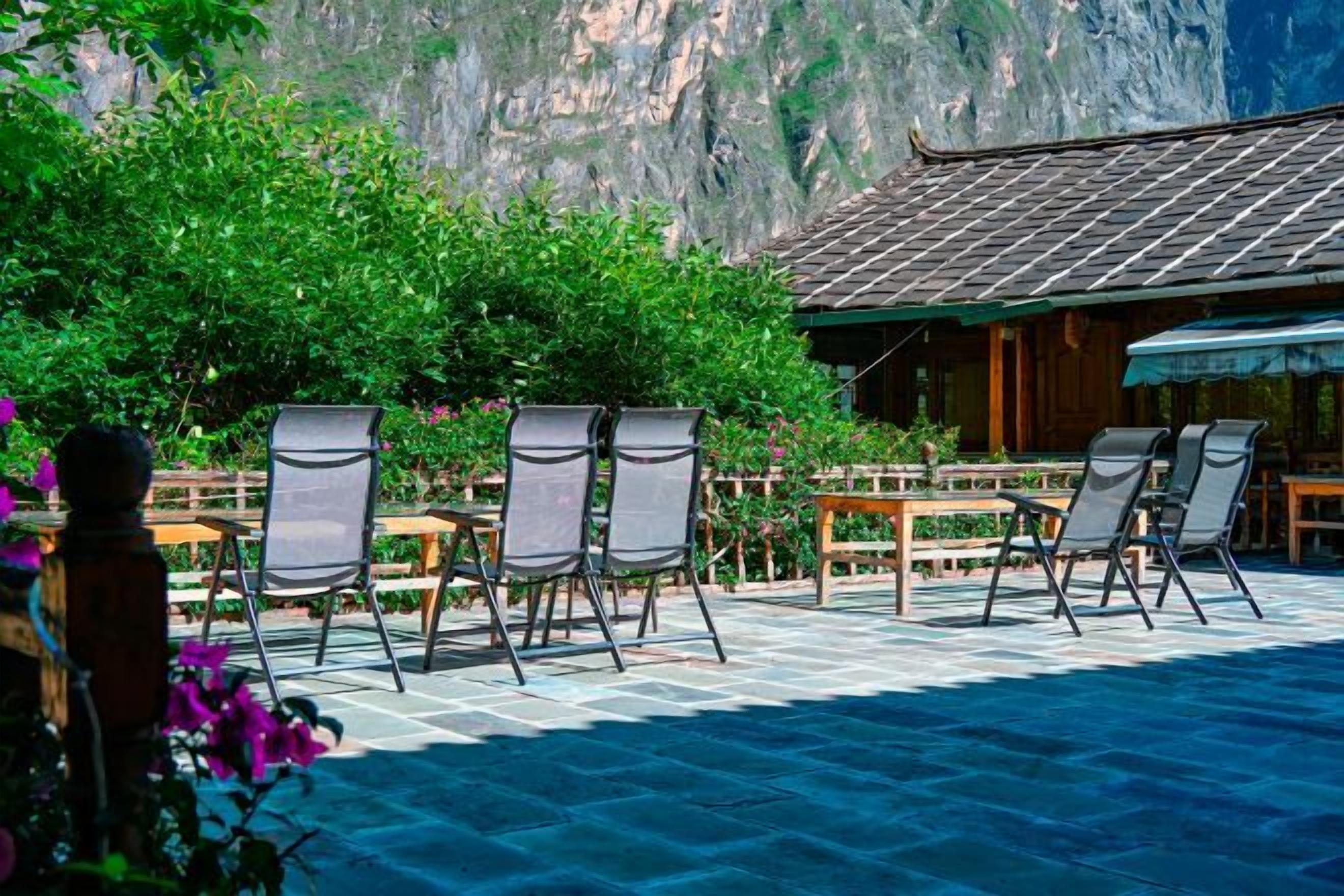 A terrace with chairs and tables, a wooden fence, and a mountain backdrop.