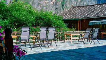 A terrace with chairs and tables, a wooden fence, and a mountain backdrop.