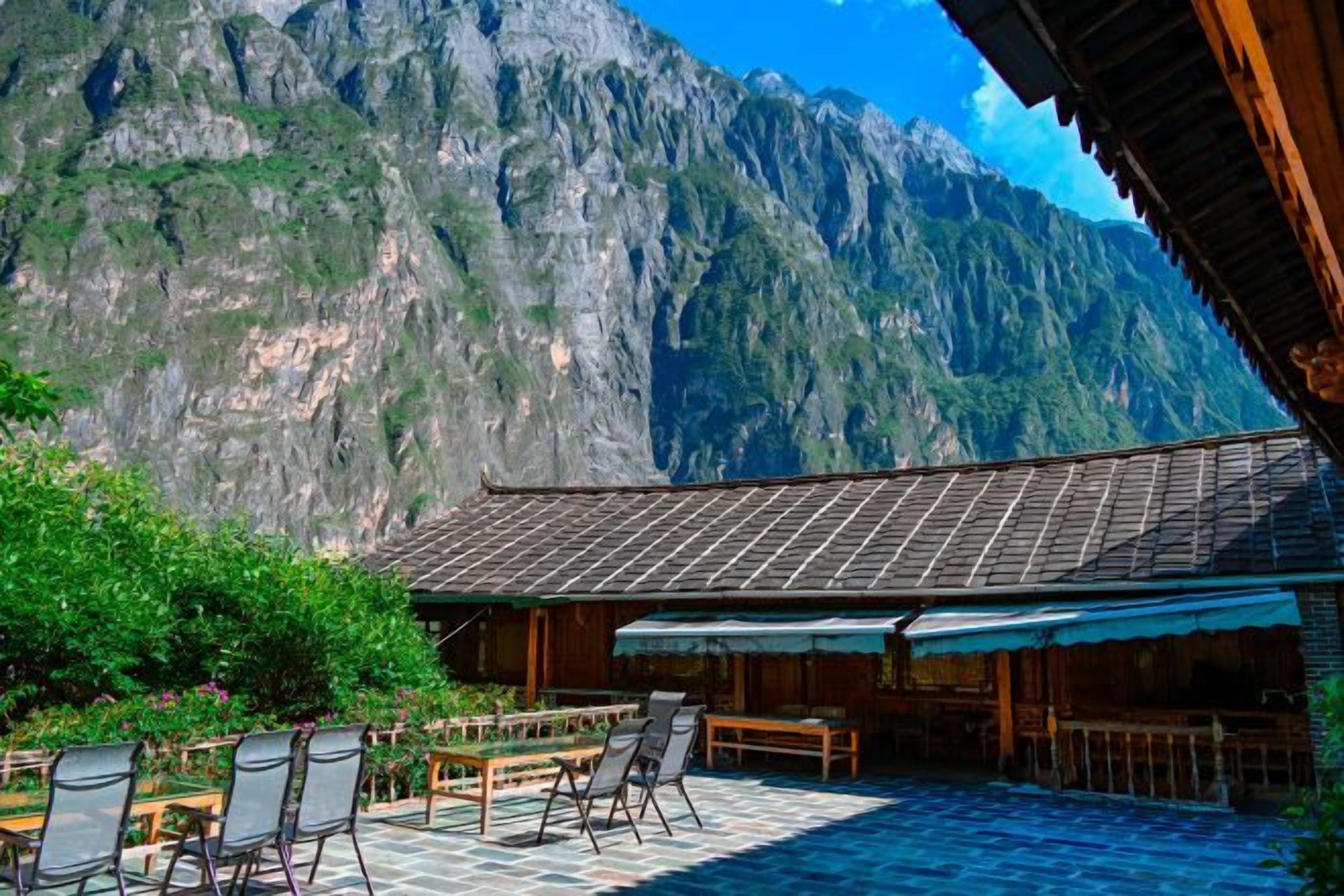 Una terraza con asientos al aire libre, un paisaje montañoso de fondo y un edificio tradicional con tejado de azulejos.