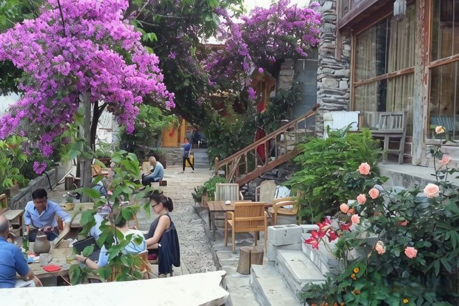 An outdoor seating area with tables and chairs, surrounded by flowering plants and a stone staircase.
