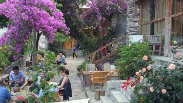 An outdoor seating area with tables and chairs, surrounded by flowering plants and a stone staircase.