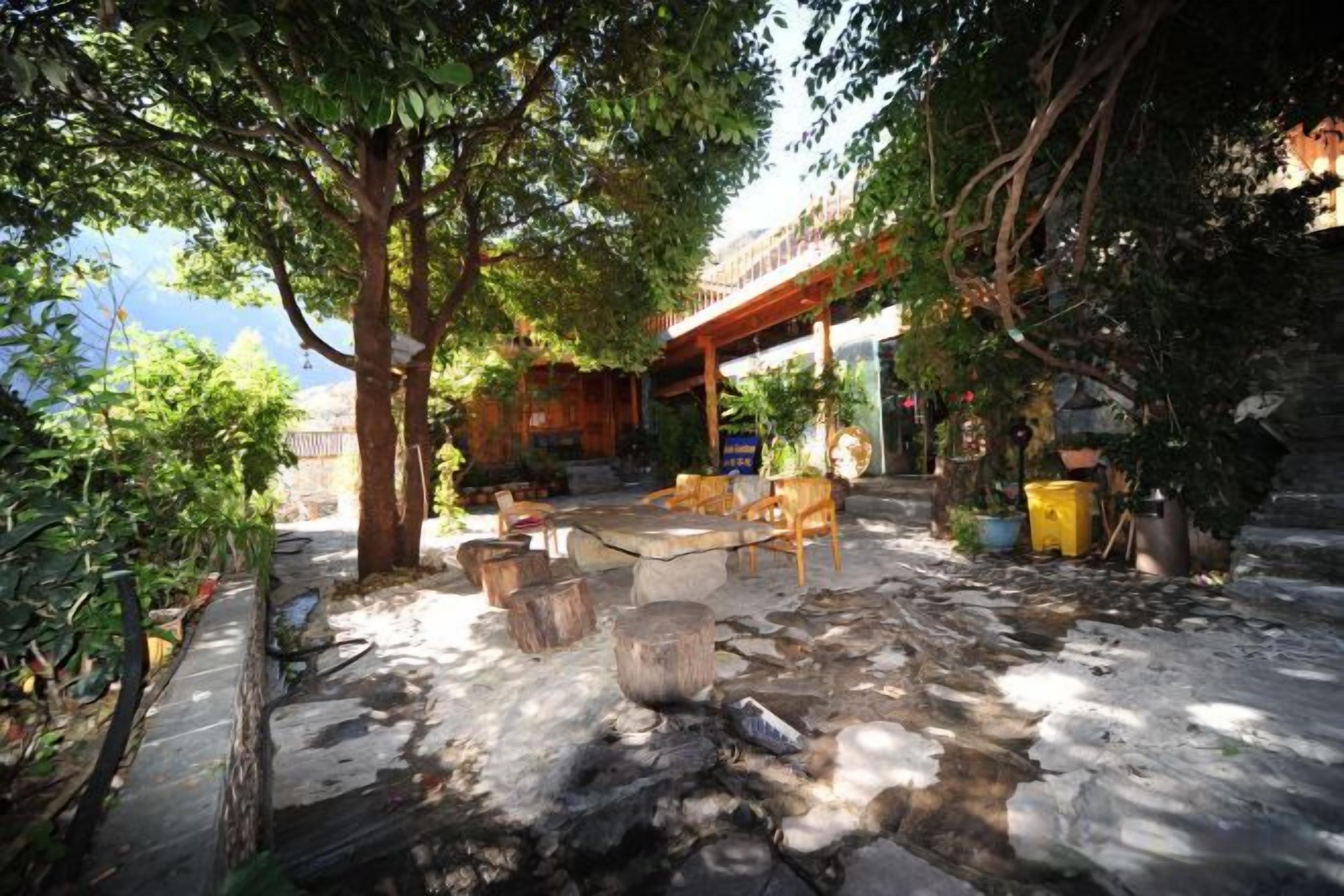 An outdoor seating area with stone flooring, wooden furniture, and potted plants.