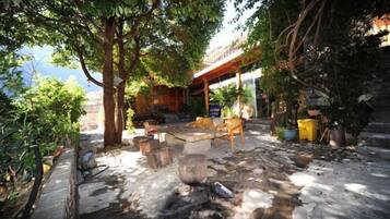 An outdoor seating area with stone flooring, wooden furniture, and potted plants.