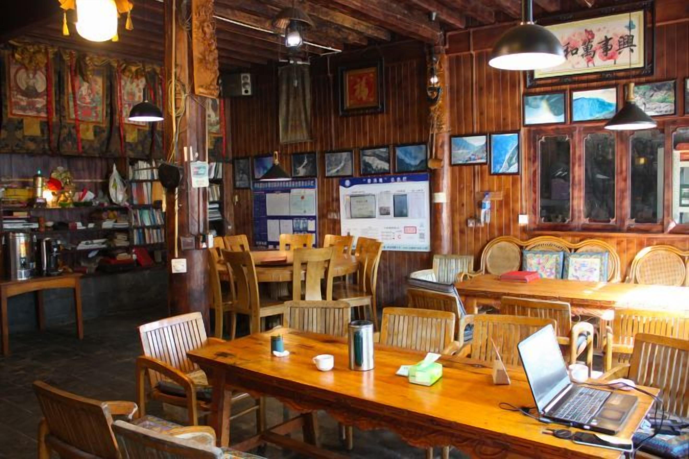 A restaurant interior with wooden furniture, tables, and chairs, and a laptop on one table.