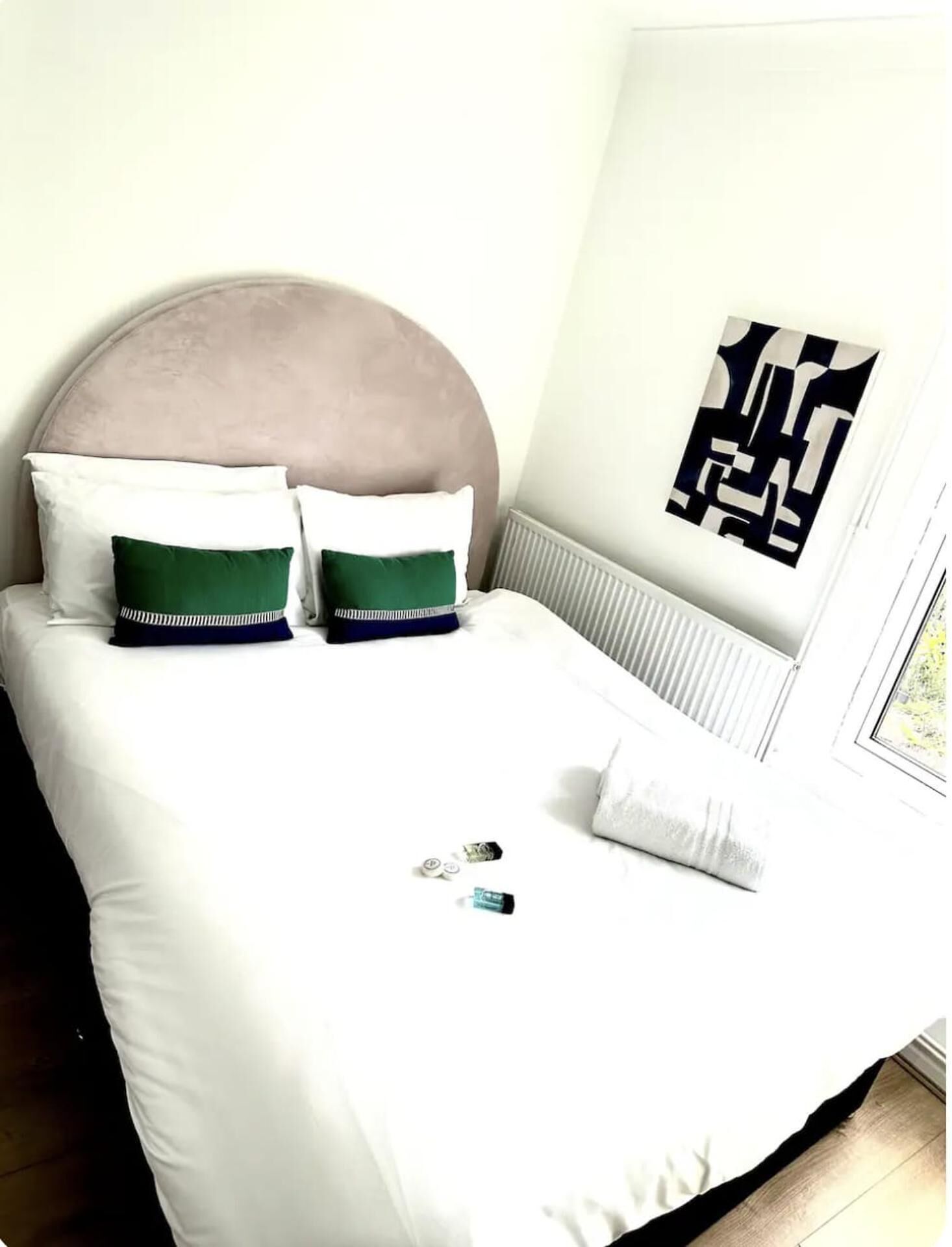 A neatly made bed with white bedding, two green and white pillows, and a beige headboard.