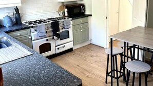 A modern kitchen with white cabinets, a granite countertop, a stove, a microwave, and a dining area with stools. - Deluxe Beach House Brighton (Brighton)