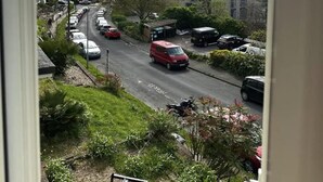 A residential street with parked cars and a red van, surrounded by greenery and buildings. - Deluxe Beach House Brighton (Brighton)