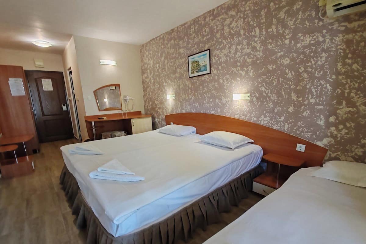 A hotel room with two beds, a wooden headboard, a wooden desk, a mirror, and a patterned wall.