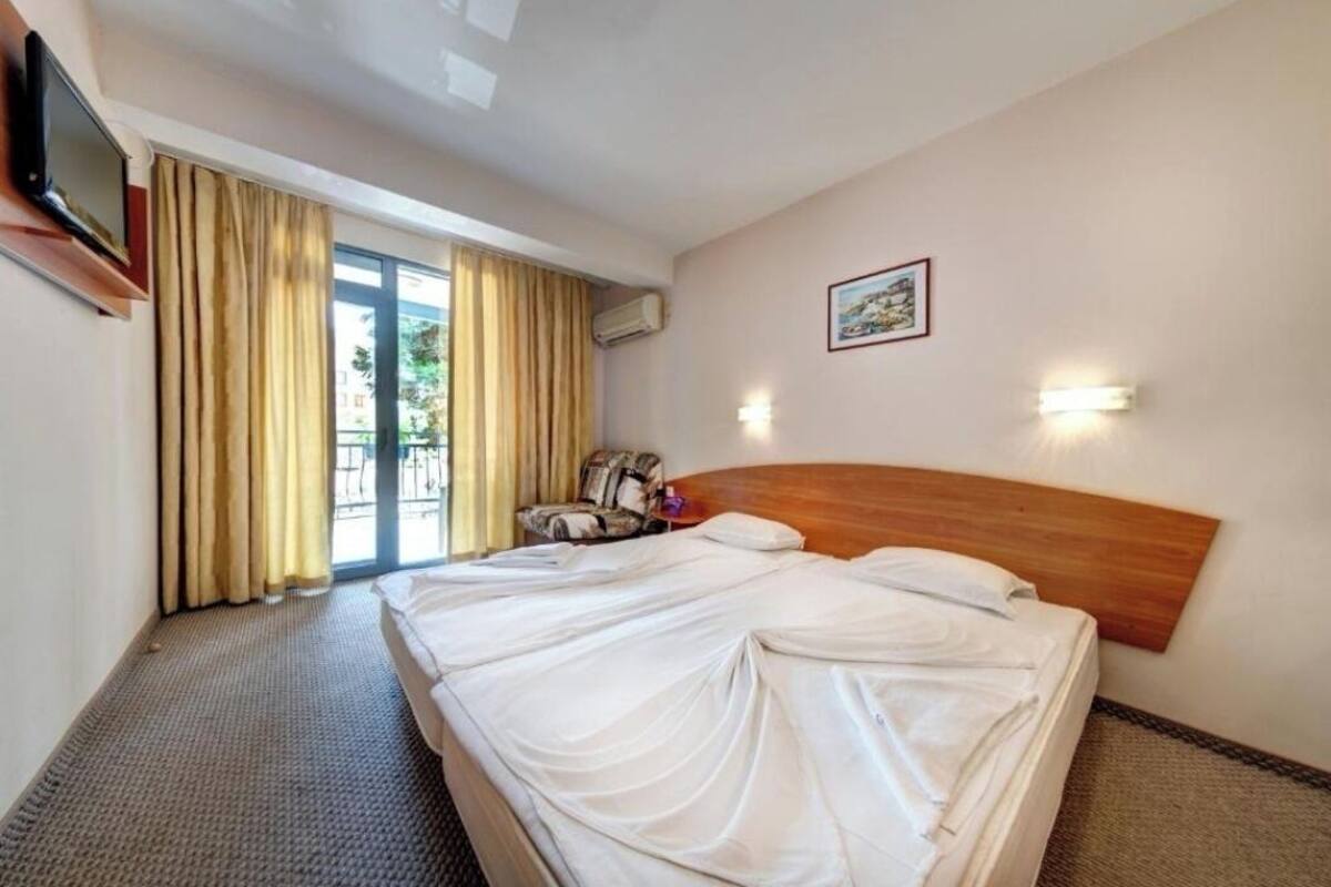 A hotel room with a large bed, a television mounted on the wall, a chair, and a window with curtains.