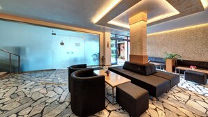 A lobby with a stone-patterned floor, a reception desk, a sofa, and a coffee table. - Hotel Paloma (Sunny Beach)