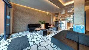 A modern lobby with stone flooring, a black sofa, a wooden coffee table, and a potted plant. - Hotel Paloma (Sunny Beach)