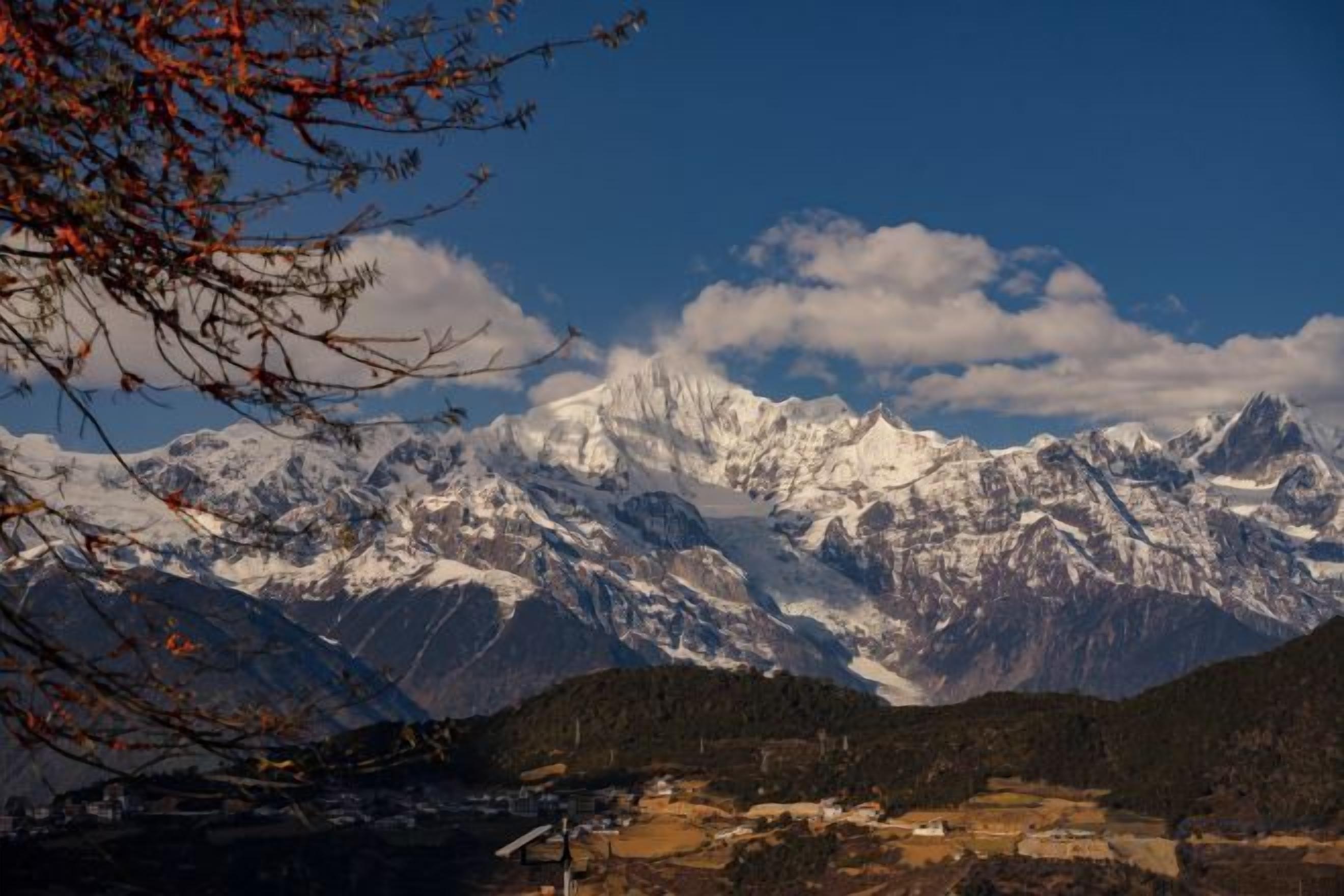 Cordillera con picos nevados, cielo despejado y valle con edificios.