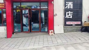 A hotel entrance with a red facade, glass doors, and a closed shutter to the right. - Shenfeng Juyuan View Hotel (Deqin)