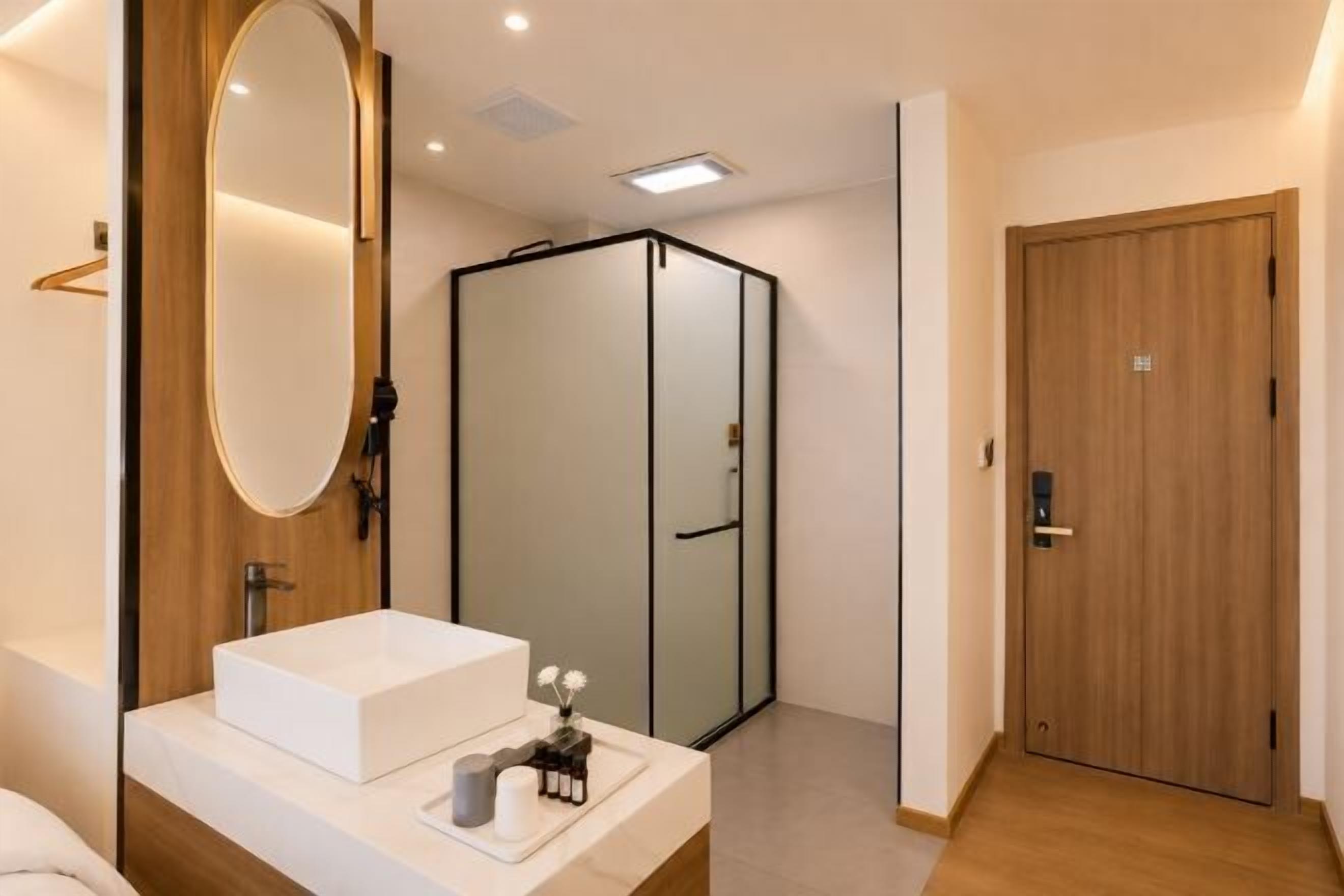 A modern bathroom with a large mirror, a white sink, and a walk-in shower.
