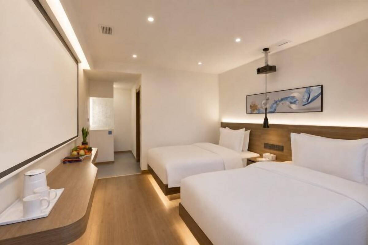 A hotel room with two beds, a bedside table, a lamp, and a painting on the wall.