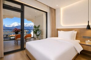 A hotel room with a bed, a desk, and a view of mountains. - Shenfeng Juyuan View Hotel (Deqin)