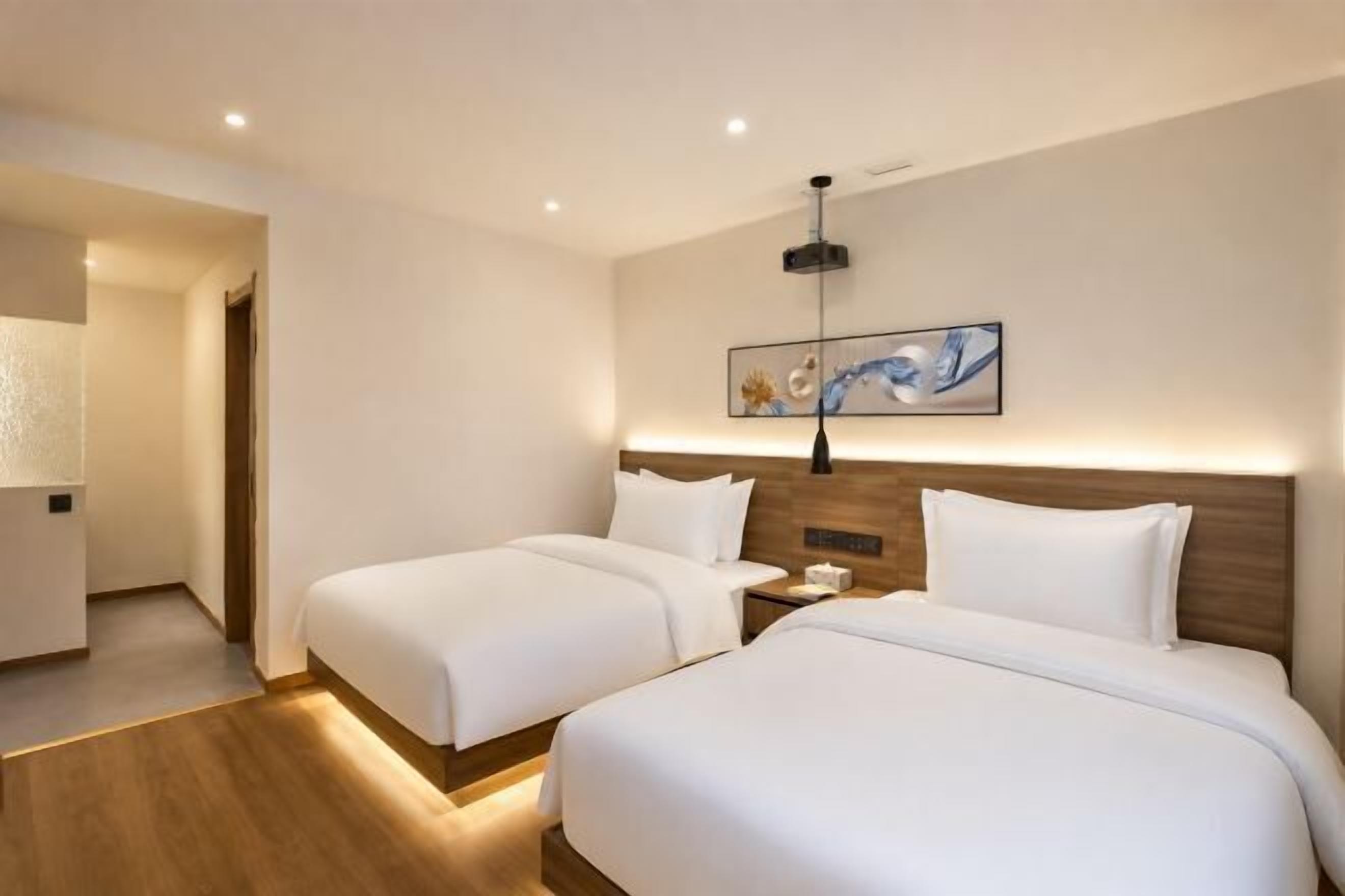A hotel room with two beds, a nightstand, a wall-mounted artwork, and a wooden floor.