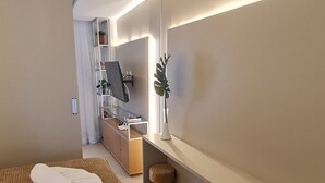 Une chambre d’hôtel avec un lit, un bureau, une chaise, un miroir et une plante.