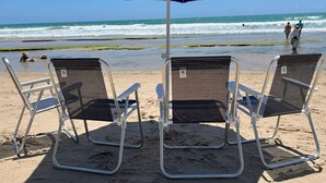 Deux chaises de plage sous un parasol bleu, sur une plage de sable, avec l’océan en arrière-plan.