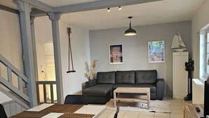 Un salon moderne comprenant un coin repas, un canapé gris, une table basse en bois et un téléviseur posé sur un meuble en bois.