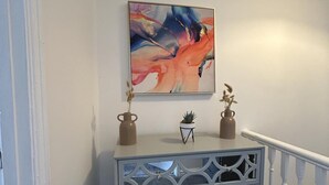 Un corridoio con un elegante tavolo consolle, un quadro astratto incorniciato e due vasi con piante essiccate.