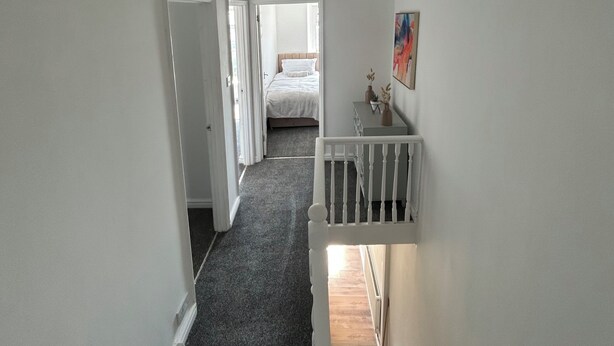 Una scala conduce a una camera da letto con un letto, un quadro appeso al muro e un piccolo tavolo con oggetti decorativi.