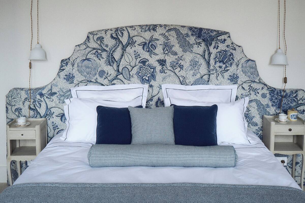 A neatly made bed with a floral headboard, two bedside tables with lamps, and a cabinet with a vase.