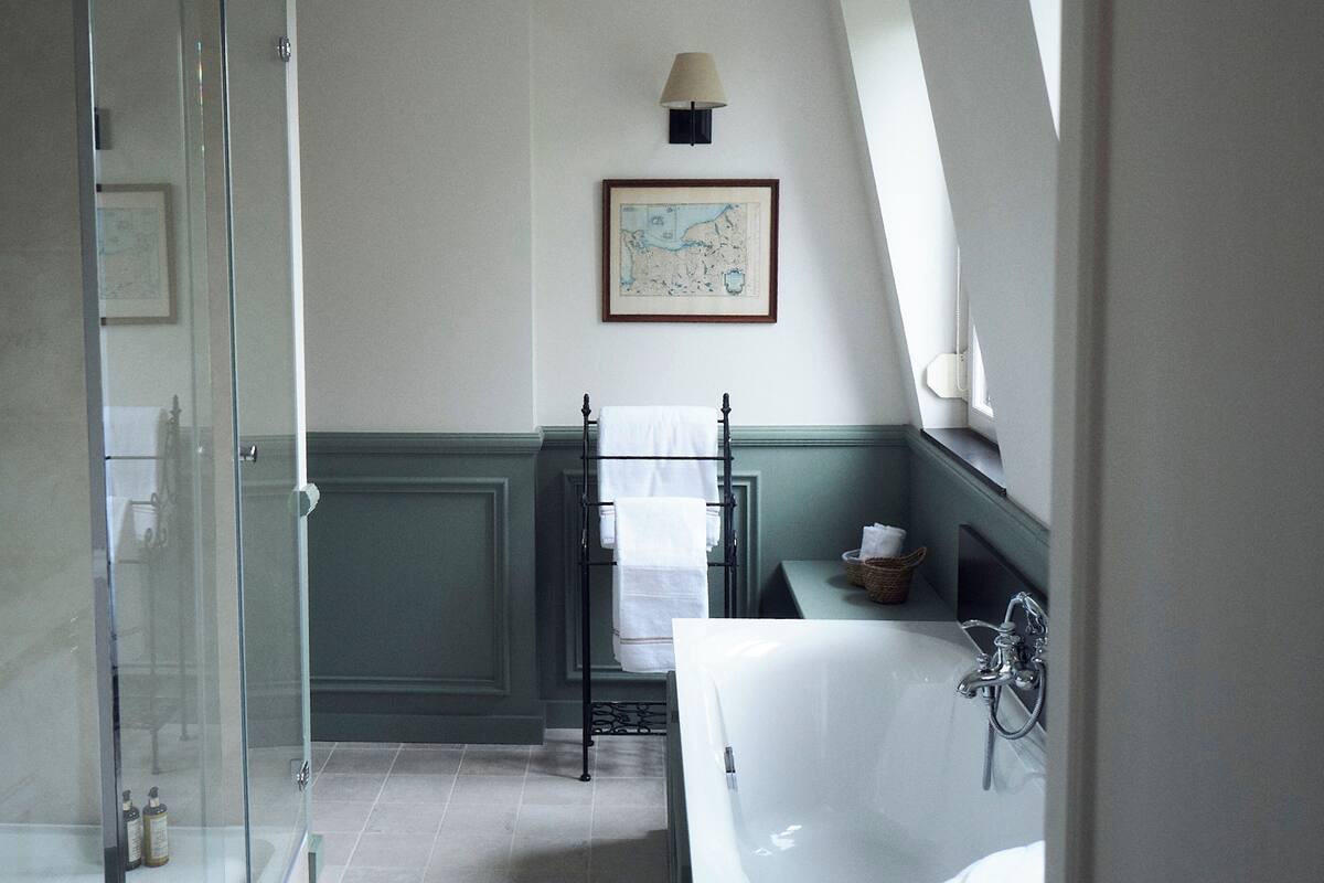 A bathroom with a glass shower enclosure, a white bathtub, and a small shelf with toiletries.