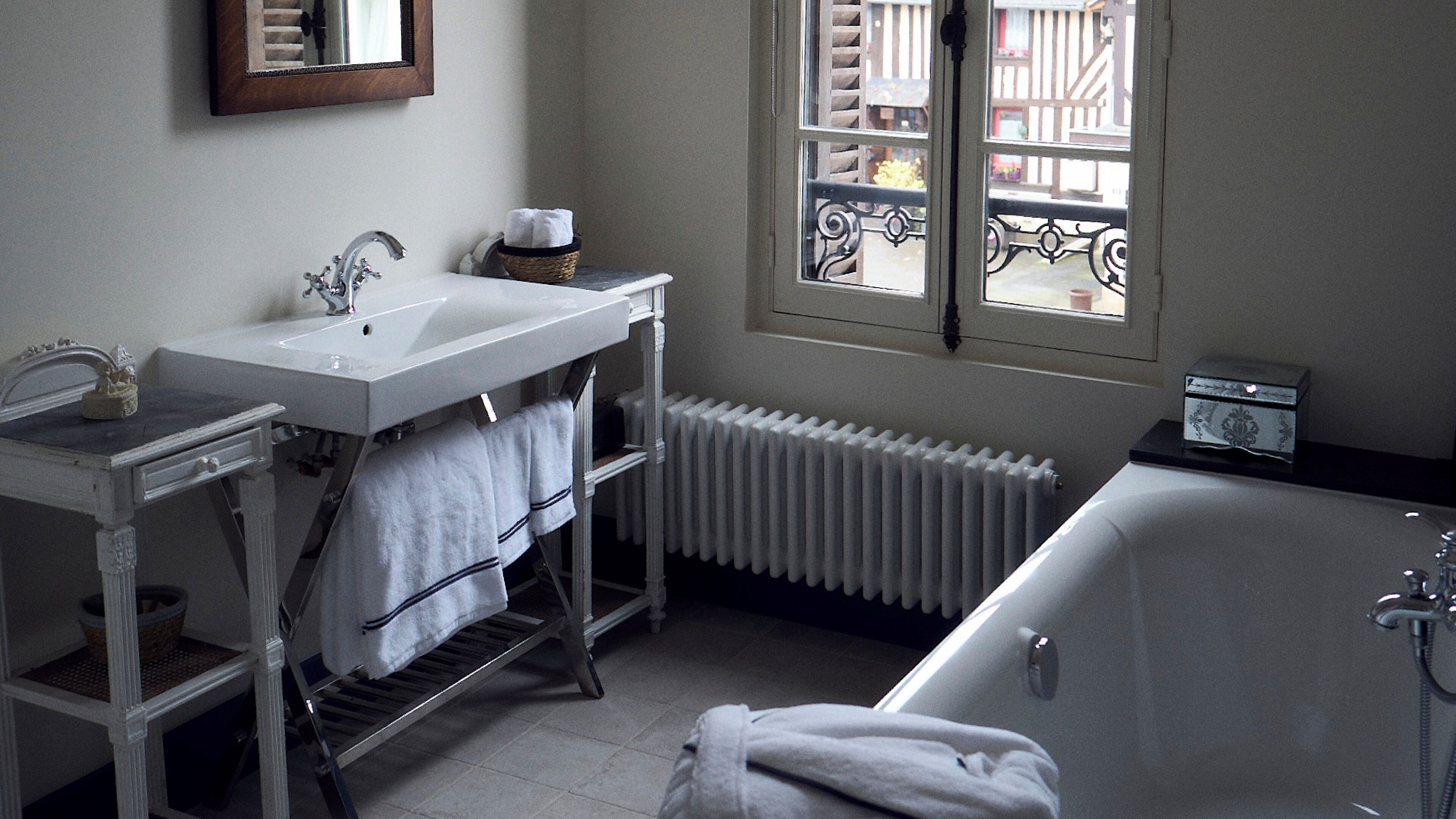 Un bany amb un lavabo blanc, una banyera i una finestra amb vista a edificis.