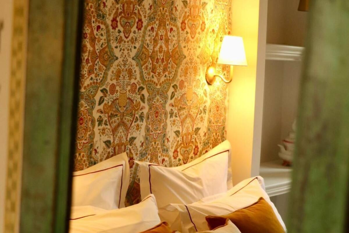 A hotel room with a bed, pillows, and a patterned wallpaper.