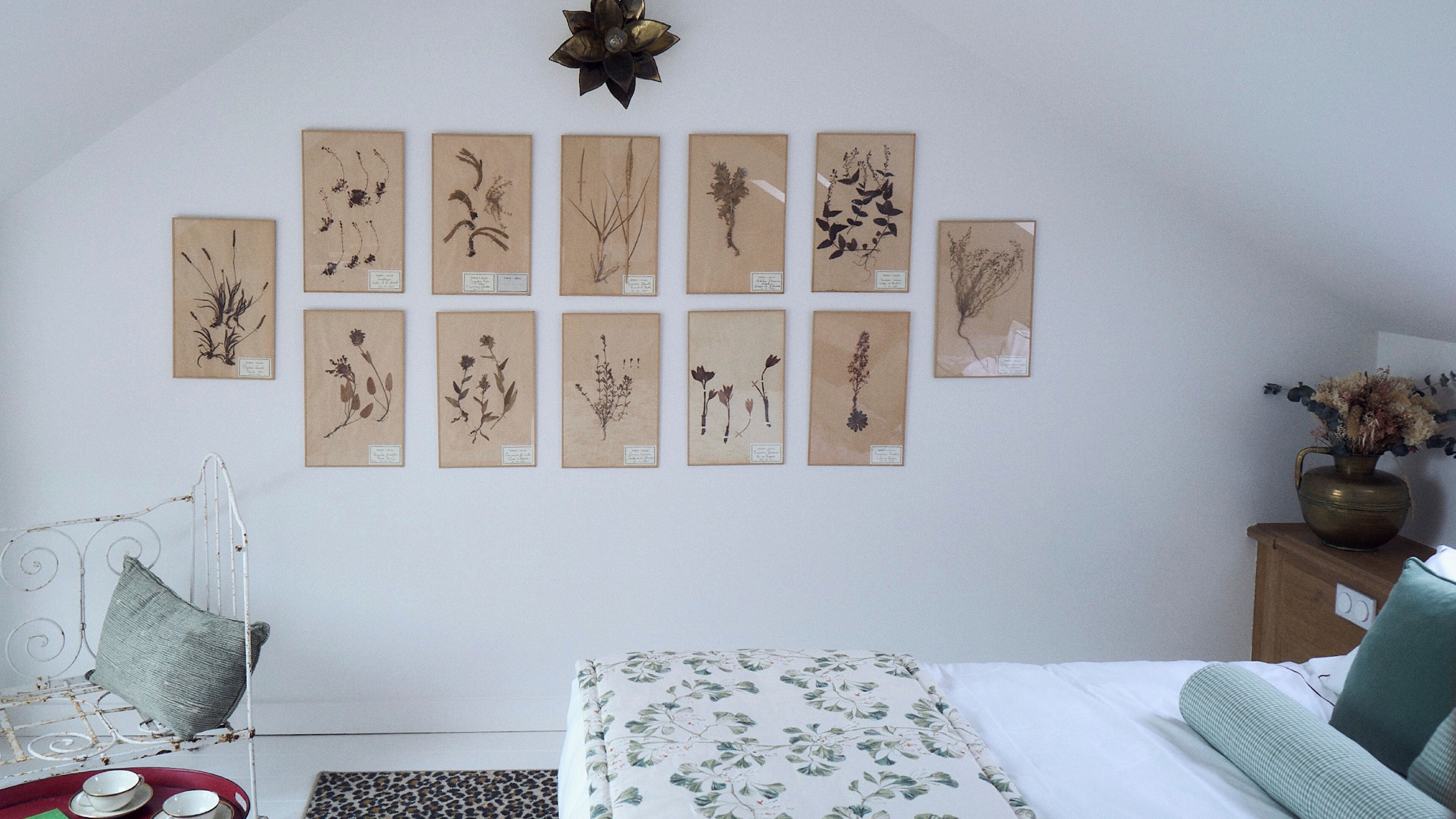 A bedroom with a bed, a nightstand, and a wall-mounted botanical illustration display.