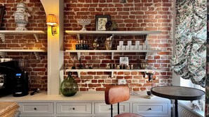 Un café acogedor con paredes de ladrillo, estantes con diversos objetos, una máquina de café y una silla.
