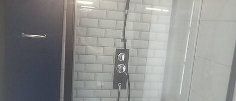 A glass-enclosed shower with a tiled wall and a control panel.