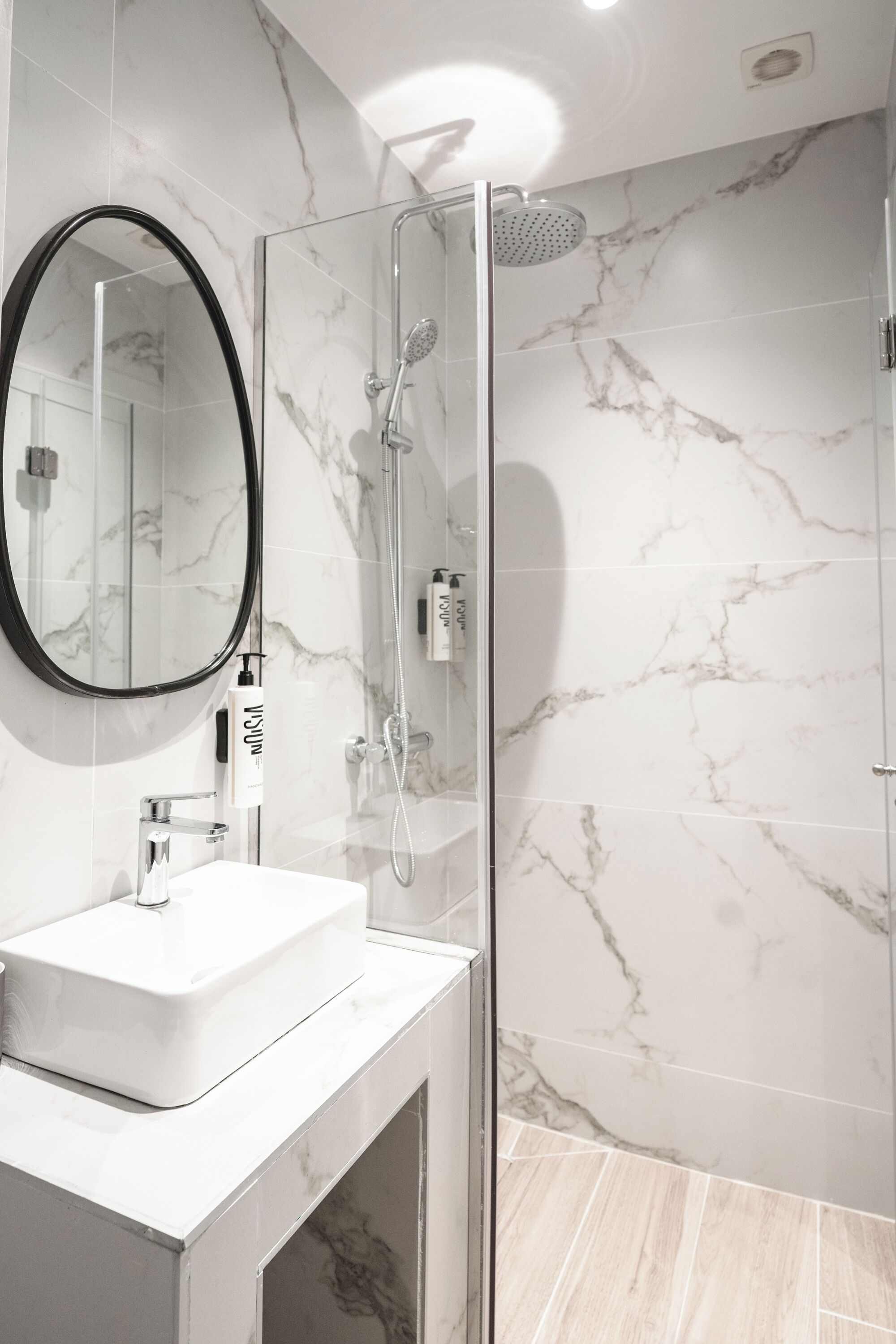 A modern bathroom with a glass-enclosed shower, a white sink, and a marble-tiled wall.
